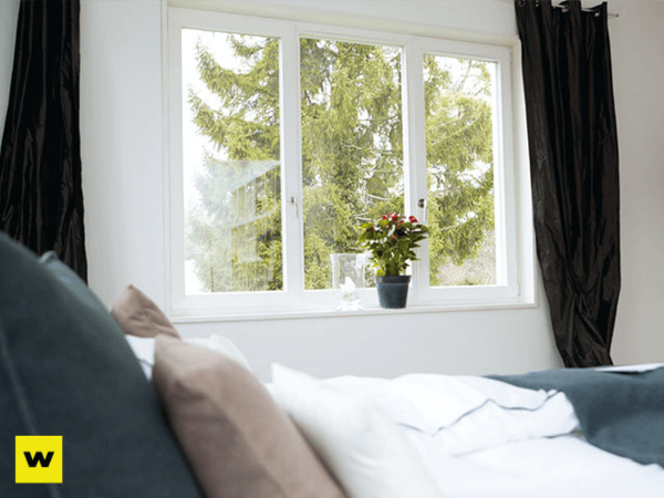 Helles Schlafzimmer mit großem Fenster, Bett und Zimmerpflanze, gemütliches Wohnen.