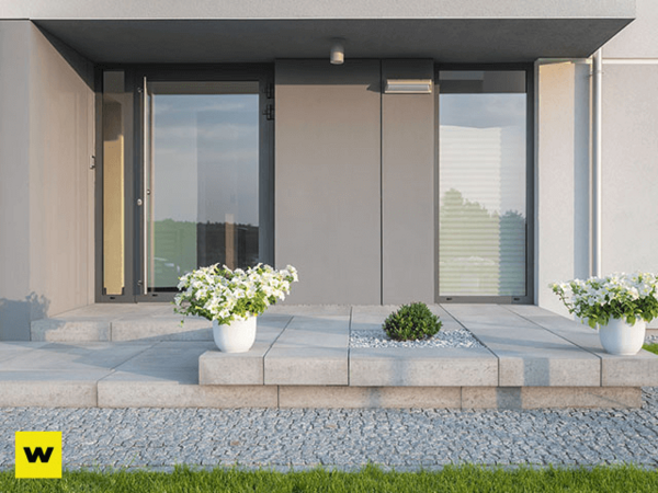 Moderner Hauseingang mit großer Glasfront, Steinplatten und bepflanzten Blumenkübeln.