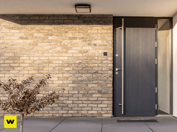 Moderne Haustür aus dunklem Material in einer Fassade aus hellen Klinkersteinen.