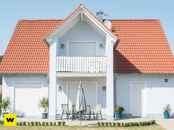 Modernes Einfamilienhaus mit rotem Dach, Balkon und geschlossener Terrasse im Garten.